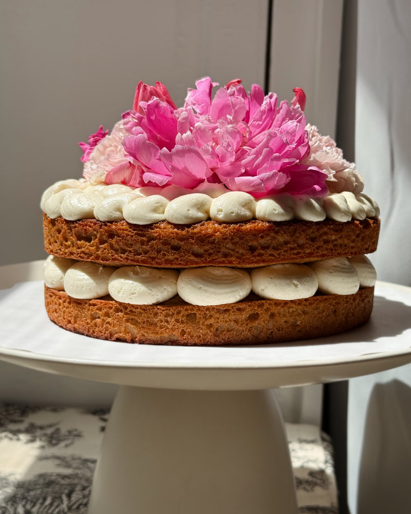 Two-layer cake with pink flowers on top, placed on a white pedestal stand. Batta all-natural cake and frosting mixes - gourmet gifts for bakers, moms, foodies