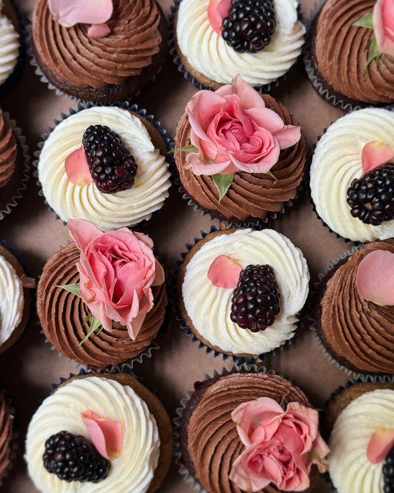 Assorted cupcakes with frosting, berries, and flowers on a dark surface. Batta all-natural cake and frosting mixes - gourmet gifts for bakers, moms, foodies